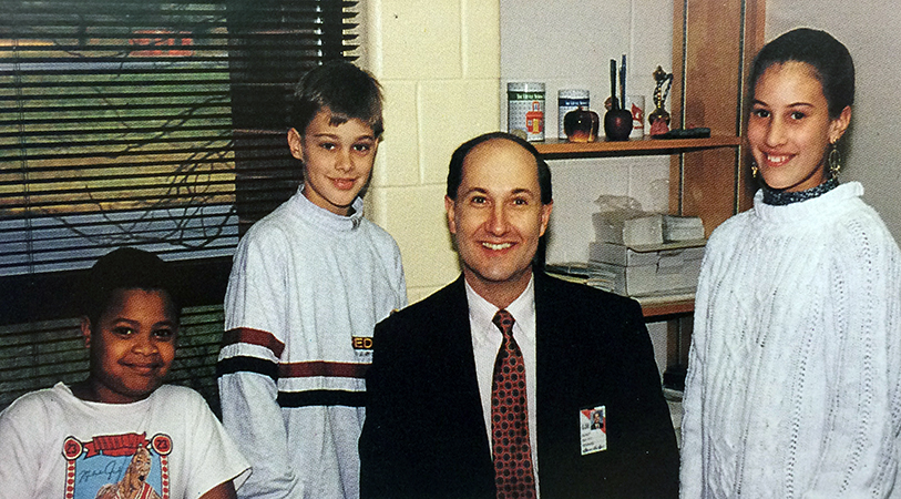 Photograph of Principal Kulp with three students taken during the 1992 to 1993 school year. They are posing for the picture in his office.