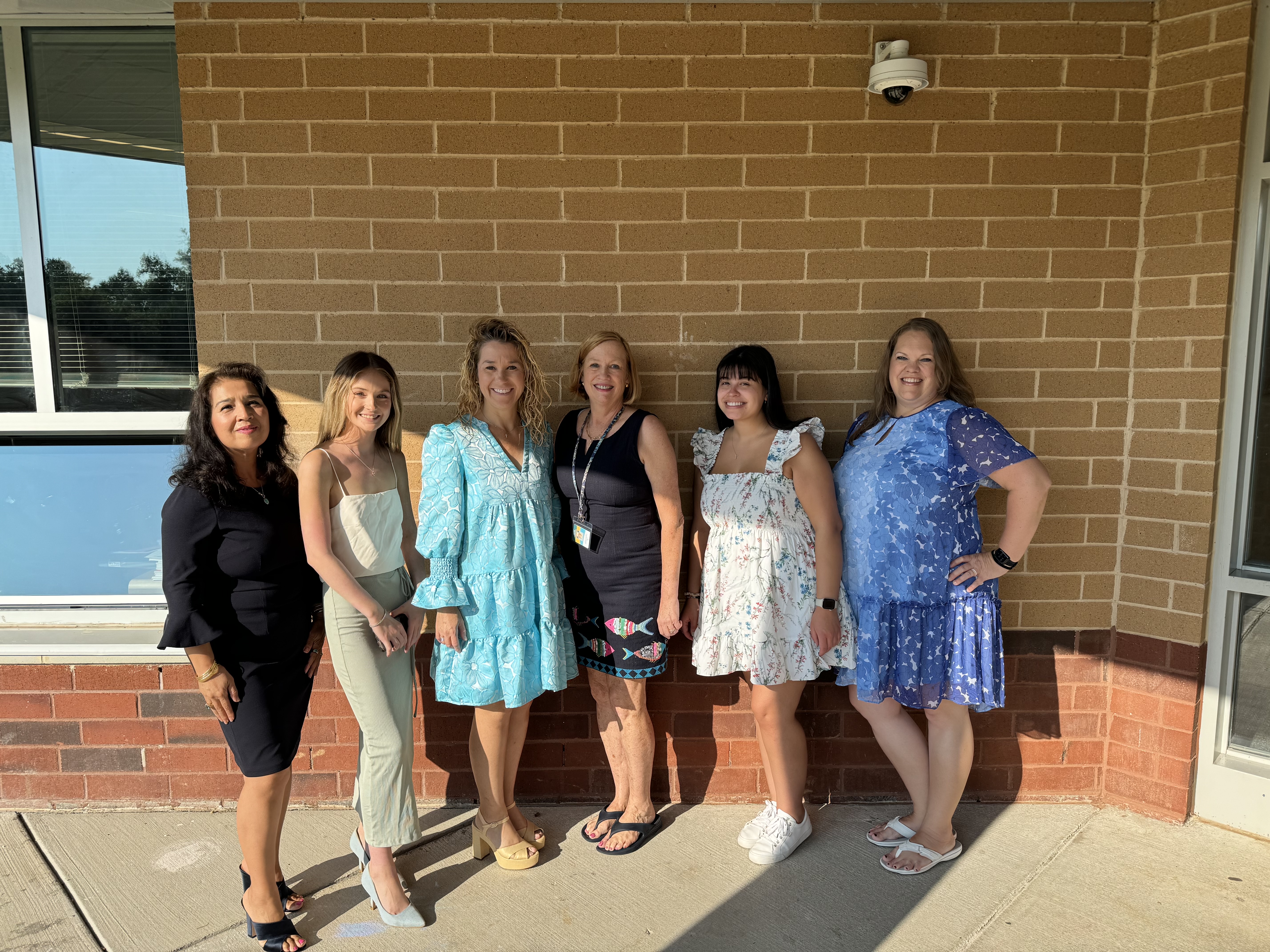 6 adult women standing outside in front of a brick wall